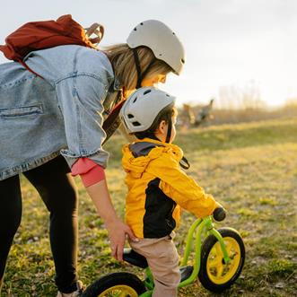 En mamma leder sitt barn på en cykel på en äng