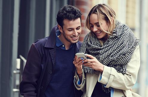 En man och en kvinna som går på en gata och kollar ner i en mobil