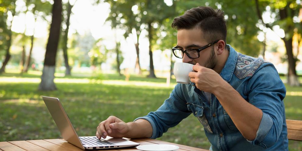 Man sitter i en park med sin laptop och dricker kaffe